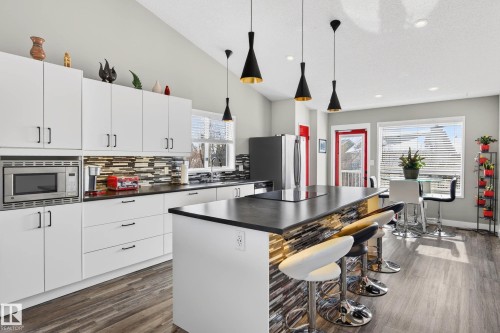 The kitchen features white cabinetry, a built-in microwave, and a large island with a cooktop and seating - 34 Donald Place, St. Albert, AB - Indoor Photo Showing Kitchen With Upgraded Kitchen