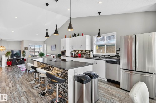 The kitchen features a large island with a stone-accented base, pendant lighting, and stainless steel appliances, including a refrigerator and dishwasher - 34 Donald Place, St. Albert, AB - Indoor