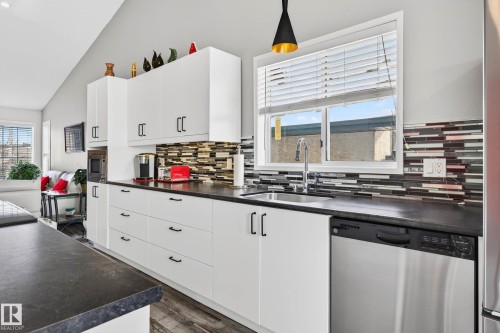 The kitchen features white cabinetry with black hardware, dark countertops, and a mosaic tile backsplash - 34 Donald Place, St. Albert, AB - Indoor Photo Showing Kitchen