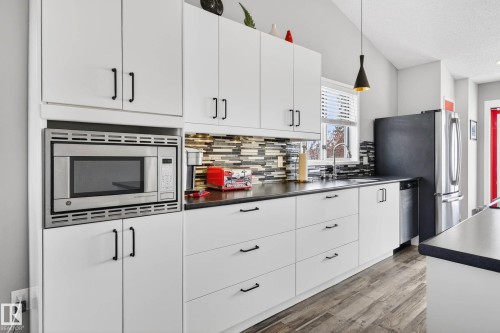 The kitchen features white cabinetry with dark hardware, black countertops, a stainless steel microwave, and a stainless steel refrigerator - 34 Donald Place, St. Albert, AB - Indoor Photo Showing Kitchen