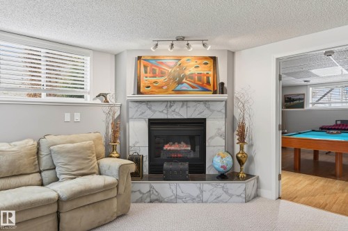 Living area featuring a fireplace with a marble-tiled hearth and surround, track lighting, and a window with blinds - 34 Donald Place, St. Albert, AB - Indoor Photo Showing Living Room With Fireplace