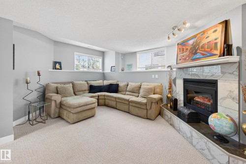 This inviting living space features carpeting, a corner sectional sofa, and a fireplace with a marble surround and hearth - 34 Donald Place, St. Albert, AB - Indoor Photo Showing Living Room With Fireplace