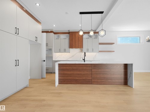 Modern kitchen featuring a large island with waterfall countertop, wood-finish paneling, and an integrated sink with a matte black faucet - 6722 Crawford Way, Edmonton, AB - Indoor Photo Showing Kitchen