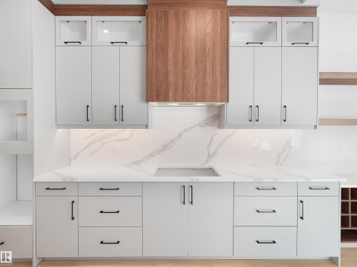 Contemporary kitchen featuring light gray cabinetry with black hardware, a wood-finish range hood, integrated cooktop, and a white countertop with a matching backsplash - 6722 Crawford Way, Edmonton, AB - Indoor Photo Showing Kitchen