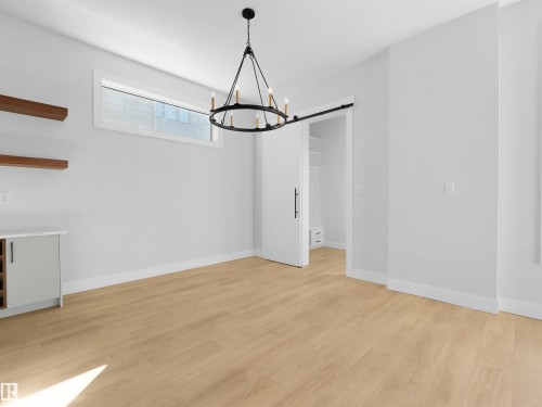 Bright open room featuring light wood-finish flooring and a contemporary black chandelier - 6722 Crawford Way, Edmonton, AB - Indoor Photo Showing Other Room