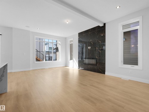 Open-concept living space featuring light wood-finish flooring, recessed lighting, and a prominent black stone-finish fireplace wall - 6722 Crawford Way, Edmonton, AB - Indoor Photo Showing Other Room