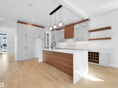 Contemporary kitchen featuring a large central island with waterfall countertop, mixed-material cabinetry, and light wood-finish flooring - 6722 Crawford Way, Edmonton, AB - Indoor Photo Showing Kitchen