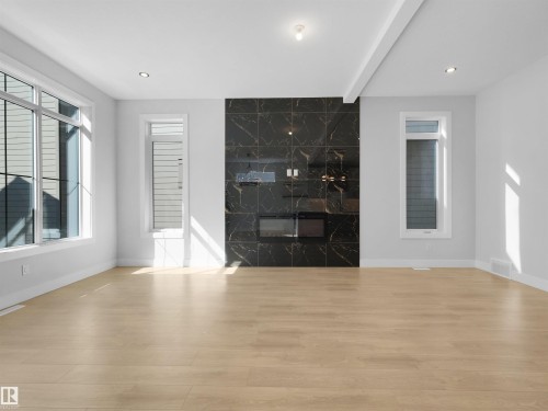 Living space featuring a full-height black marble-patterned fireplace surround, an electric fireplace insert, and a recessed television niche - 6722 Crawford Way, Edmonton, AB - Indoor