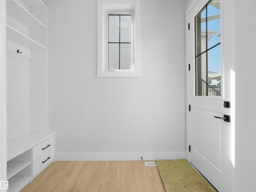 Entryway featuring wood-finish flooring, a white paneled door with a grid-patterned glass insert, and a built-in mudroom bench with open shelving, drawers, and coat hooks - 6722 Crawford Way, Edmonton, AB - Indoor Photo Showing Other Room