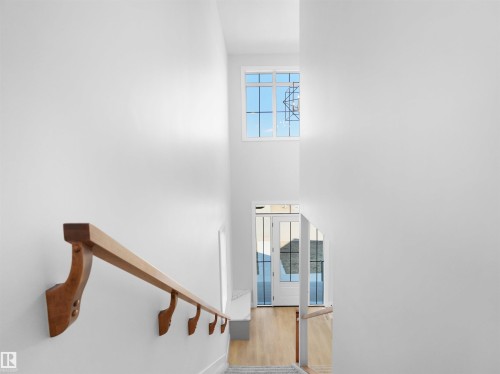 Bright stairwell featuring a wood handrail with decorative brackets, a tall window with grid panes, and a contemporary geometric light fixture - 6722 Crawford Way, Edmonton, AB - Indoor Photo Showing Other Room