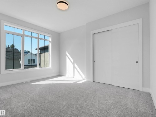Light gray wall paint featuring a large multi-pane window, white baseboards, and gray carpet flooring - 6722 Crawford Way, Edmonton, AB - Indoor Photo Showing Other Room