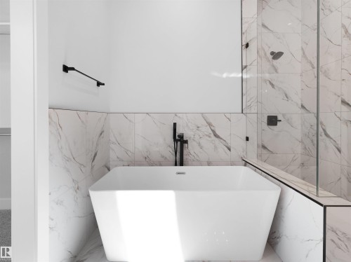 Freestanding soaking tub with matte black fixtures, marble-look wall tiling, and a frameless glass shower enclosure - 6722 Crawford Way, Edmonton, AB - Indoor Photo Showing Bathroom