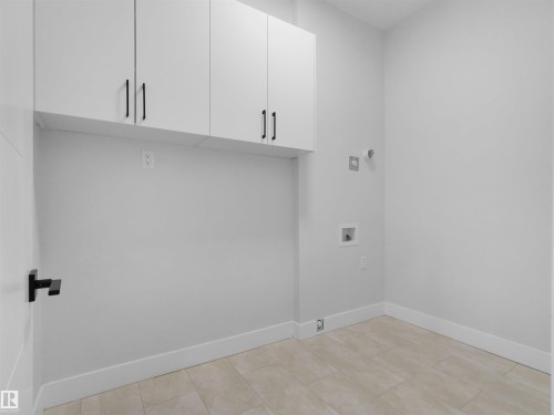 Laundry area featuring upper cabinetry with modern hardware, light tile flooring, and white baseboards - 6722 Crawford Way, Edmonton, AB - Indoor Photo Showing Other Room