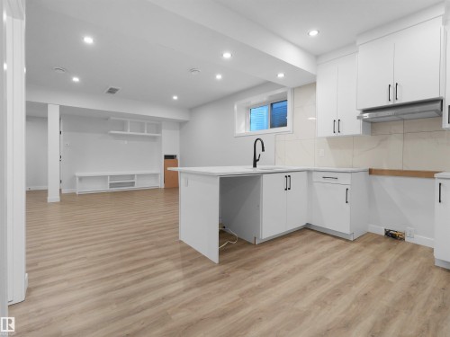 Modern kitchen featuring white cabinetry, a black gooseneck faucet, light-toned backsplash, and a coordinating range hood - 6722 Crawford Way, Edmonton, AB - Indoor Photo Showing Kitchen