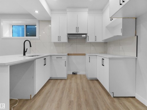 Modern kitchen featuring white cabinetry, quartz countertops, a matte black gooseneck faucet, light-toned wood-finish flooring, and a tiled backsplash - 6722 Crawford Way, Edmonton, AB - Indoor Photo Showing Kitchen