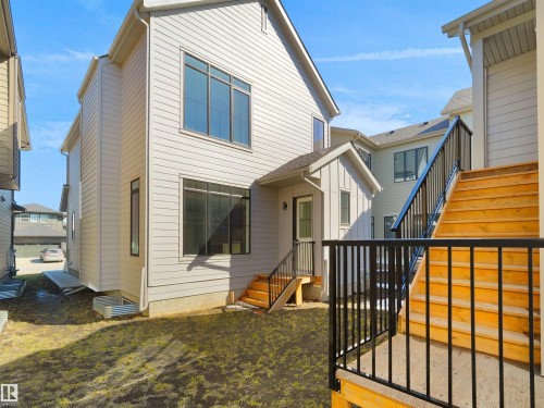 Modern siding exterior with multiple window configurations, a rear entry door, and wooden stairs with black metal railings - 6722 Crawford Way, Edmonton, AB - Outdoor With Exterior