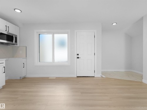 Open-concept space featuring light wood-finish flooring, recessed lighting, and a kitchen area with white cabinetry, stainless steel microwave, and light-toned backsplash - 6722 Crawford Way, Edmonton, AB - Indoor Photo Showing Other Room