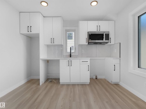 Modern kitchen featuring white shaker-style cabinetry, a stainless steel microwave, matte black faucet, light-toned wood-finish flooring, and recessed ceiling lighting - 6722 Crawford Way, Edmonton, AB - Indoor Photo Showing Kitchen