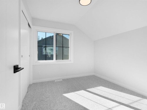 Bedroom featuring light gray carpeting, crisp white walls, a large window with gridded panes, a modern flush-mount ceiling light, and a white sliding closet door with a matte black handle - 6722 Crawford Way, Edmonton, AB - Indoor Photo Showing Other Room
