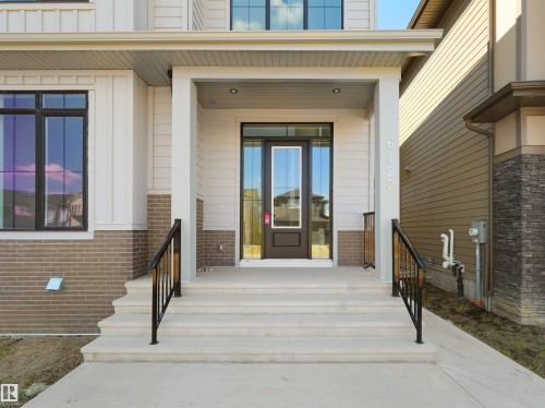 Inviting front entrance featuring a dark-framed glass panel door, concrete steps with black railings, and a covered porch - 6722 Crawford Way, Edmonton, AB - Outdoor With Exterior