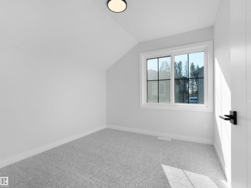 Bright room featuring a window with black grilles, light gray carpeting, and a white door with matte black hardware - 6722 Crawford Way, Edmonton, AB - Indoor Photo Showing Other Room