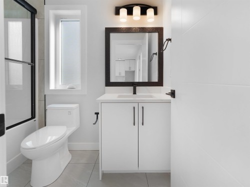 Modern bathroom featuring a white vanity with a light-toned countertop, a rectangular mirror with dark trim, and a three-light fixture - 6722 Crawford Way, Edmonton, AB - Indoor Photo Showing Bathroom