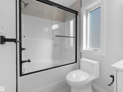 Modern bathroom featuring a bathtub with a sliding glass door and matte black frame, complemented by a coordinating matte black showerhead and faucet - 6722 Crawford Way, Edmonton, AB - Indoor Photo Showing Bathroom