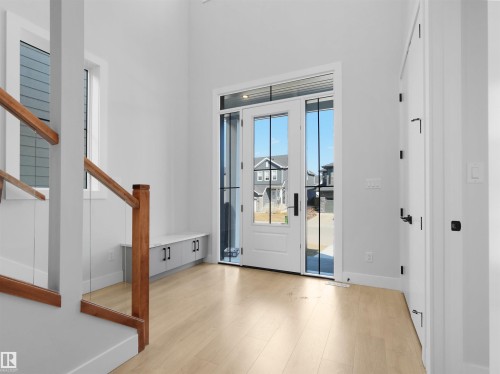 Entryway featuring a double-pane glass door with sidelights, light wood-finish flooring, a built-in storage bench, a staircase with wood handrails and glass panels, and a high ceiling - 6722 Crawford Way, Edmonton, AB - Indoor Photo Showing Other Room
