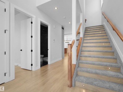 Hardwood-finish flooring extending through the entry, with a staircase featuring carpeted treads, wood risers, and integrated lighting - 6722 Crawford Way, Edmonton, AB - Indoor Photo Showing Other Room