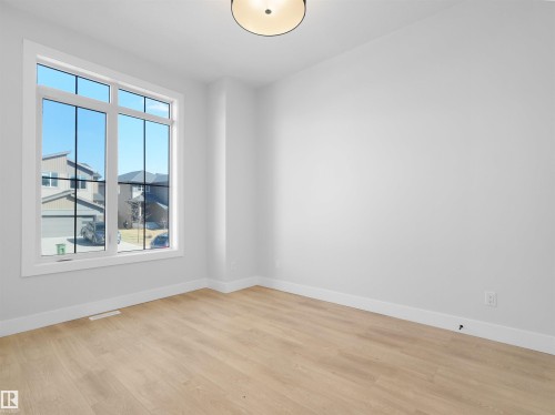 Spacious room featuring a large multi-pane window, light wood-finish flooring, white baseboards, and a contemporary flush-mount ceiling light fixture - 6722 Crawford Way, Edmonton, AB - Indoor Photo Showing Other Room
