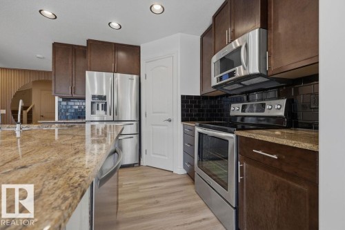 Kitchen featuring dark wood cabinetry, stainless steel appliances, black subway tile backsplash, and light wood-finish flooring - Edmonton, AB - Indoor Photo Showing Kitchen With Stainless Steel Kitchen With Upgraded Kitchen