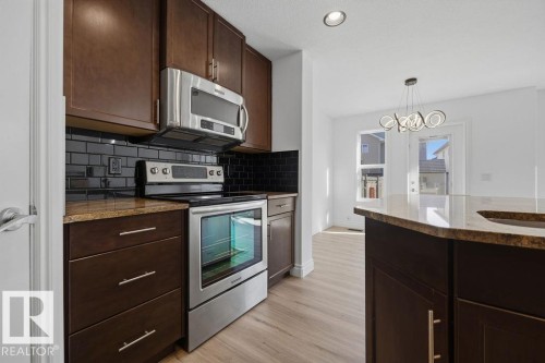 Kitchen featuring stainless steel appliances, dark wood-finish cabinetry, and a black subway tile backsplash - Edmonton, AB - Indoor Photo Showing Kitchen