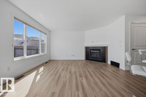 Spacious living area featuring expansive windows, wood-finish flooring, a corner fireplace with a tiled surround, and white baseboards - Edmonton, AB - Indoor Photo Showing Living Room With Fireplace
