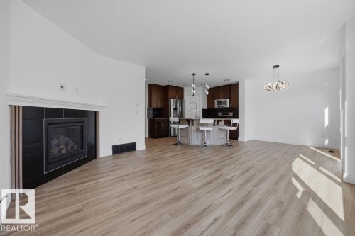 Spacious living area featuring wood-finish flooring, a black tiled fireplace with a white mantel, and a contemporary chandelier - Edmonton, AB - Indoor Photo Showing Living Room With Fireplace