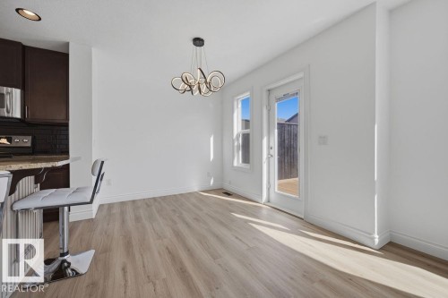 Open-concept dining area featuring wood-finish flooring, a contemporary chandelier, and a white framed door with an adjacent window providing outdoor access - Edmonton, AB - Indoor