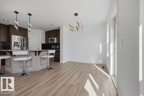Kitchen featuring dark wood cabinetry, stainless steel appliances, a light-toned countertop island with pendant lighting, and wood-finish flooring throughout - Edmonton, AB - Indoor Photo Showing Kitchen With Upgraded Kitchen