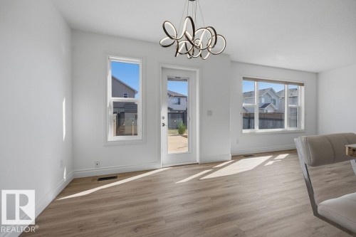 Spacious room featuring wood-finish flooring, white baseboards, and a contemporary chandelier - Edmonton, AB - Indoor Photo Showing Other Room