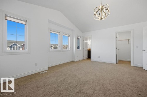 Spacious room featuring vaulted ceilings, light-colored carpeting, multiple windows, a modern overhead light fixture, and two interior doorways - Edmonton, AB - Indoor Photo Showing Other Room