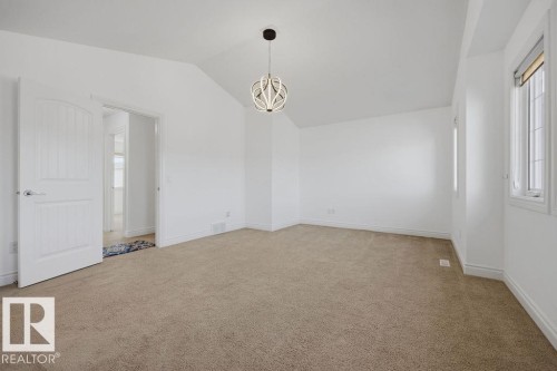 Spacious room featuring vaulted ceilings, a contemporary pendant light fixture, and neutral carpeting - Edmonton, AB - Indoor Photo Showing Other Room