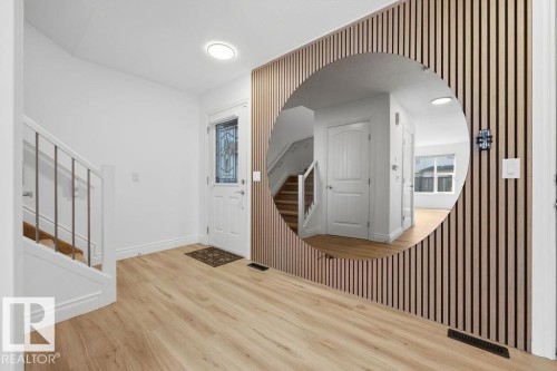 Entryway featuring light wood-finish flooring, a white paneled front door with decorative glass, and a modern accent wall with vertical wood slat detailing - Edmonton, AB - Indoor Photo Showing Other Room