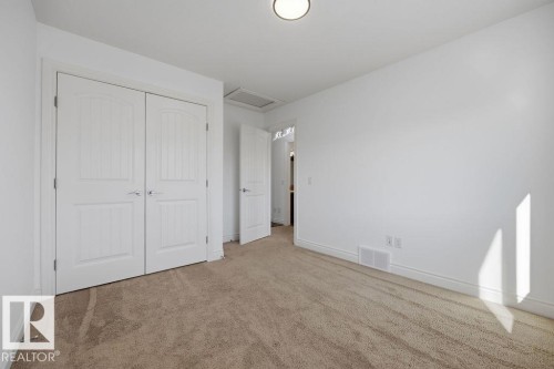 Carpeted room featuring a double-door closet with arch-top paneling, a flush-mount ceiling light fixture, and white painted trim - Edmonton, AB - Indoor Photo Showing Other Room