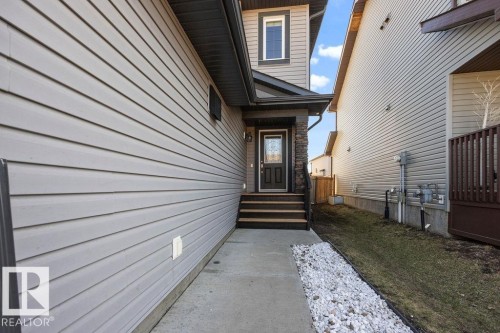 Front entry featuring stacked stone accents, a dark wood-finish door with decorative glass, and wood-finish steps - Edmonton, AB - Outdoor With Exterior