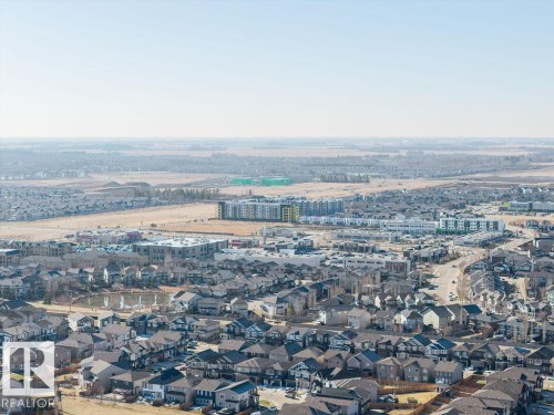Aerial perspective of a developing residential area featuring multiple housing styles, a central pond, and commercial structures - Edmonton, AB - Outdoor With View