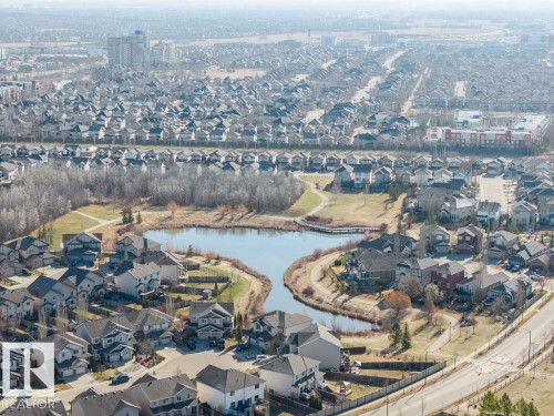 Aerial perspective showcasing a residential community with numerous single-family homes, a central pond, and surrounding parkland - Edmonton, AB - Outdoor With Body Of Water With View