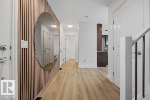 Entryway featuring a wood-slat accent wall with a circular mirror, wood-finish flooring, white doors, and a staircase with white newel posts and dark balusters - Edmonton, AB - Indoor Photo Showing Other Room