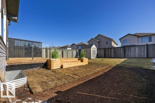 Expansive backyard featuring a large wooden deck with glass panel railing, a lawn area, and a storage shed - Edmonton, AB - Outdoor