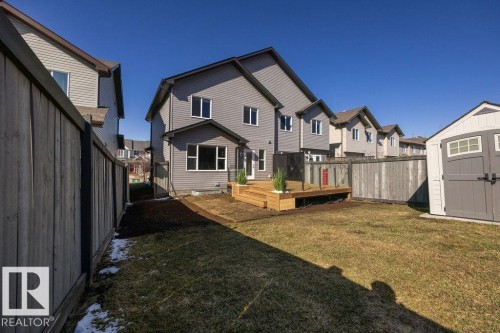 Rear exterior with a wooden deck featuring glass panel railings, a detached shed, horizontal siding, and multiple windows - Edmonton, AB - Outdoor
