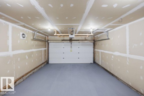 Spacious garage featuring a light gray floor, white panel garage door, built-in overhead storage system, and exposed drywall - Edmonton, AB - Indoor Photo Showing Garage