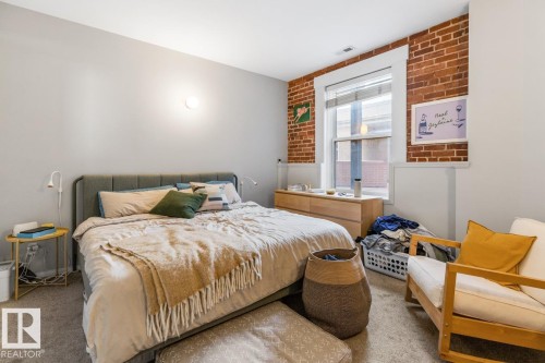 Exposed brick accent wall and a large window with white trim - 109 10728 82 Avenue, Edmonton, AB - Indoor Photo Showing Bedroom