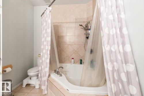 Bathroom featuring a corner jetted tub with integrated shower, tiled surround, and a toilet - 109 10728 82 Avenue, Edmonton, AB - Indoor Photo Showing Bathroom
